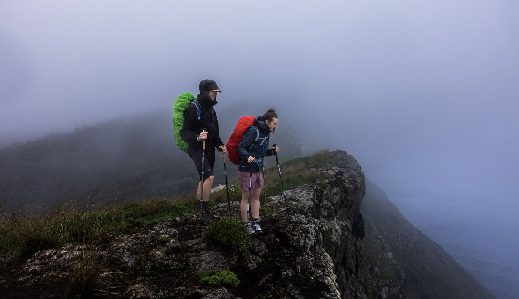 Twee personen staan in de mist op een klif. 