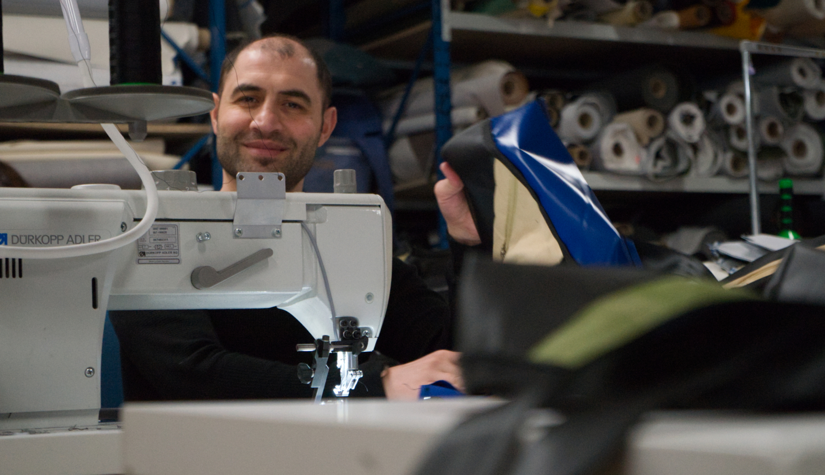 Een lachende man zit achter een naaimachine en laat zien hoe hij een tas maakt 