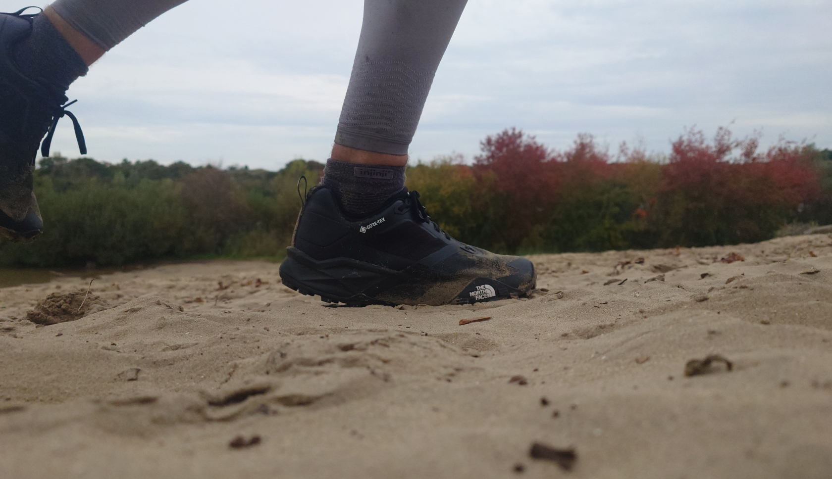 een man loopt op trailschoenen van the north face in de duinen