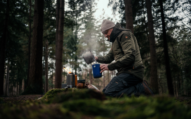 een persoon schenkt een kop koffie in in de bossen