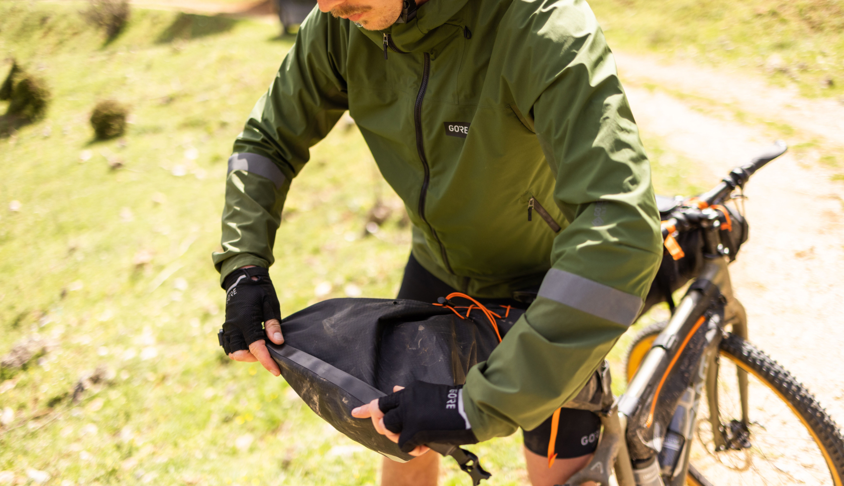 Een man rolt een tas dicht die achter zijn fietszadel is bevestigd