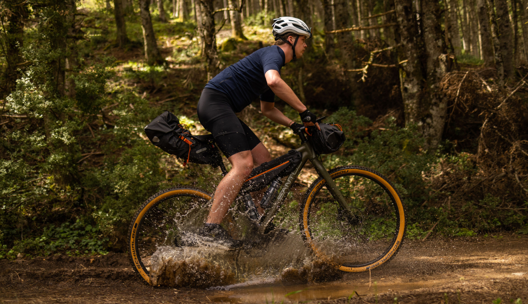 Een man fietst door een plas in het bos en water spat op naar zijn benen