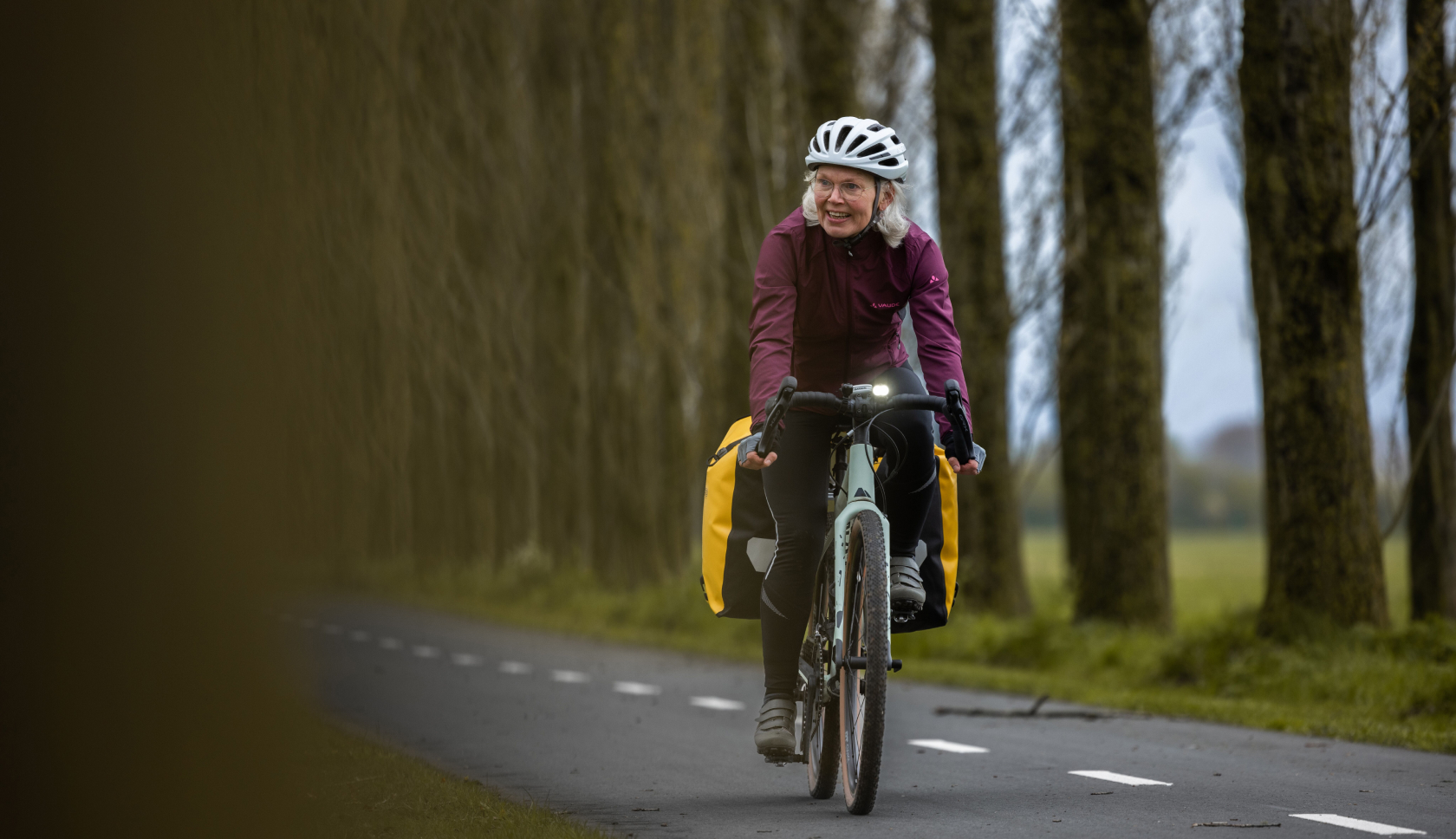 een oudere vrouw fietst over een weg waarlangs bomen staan