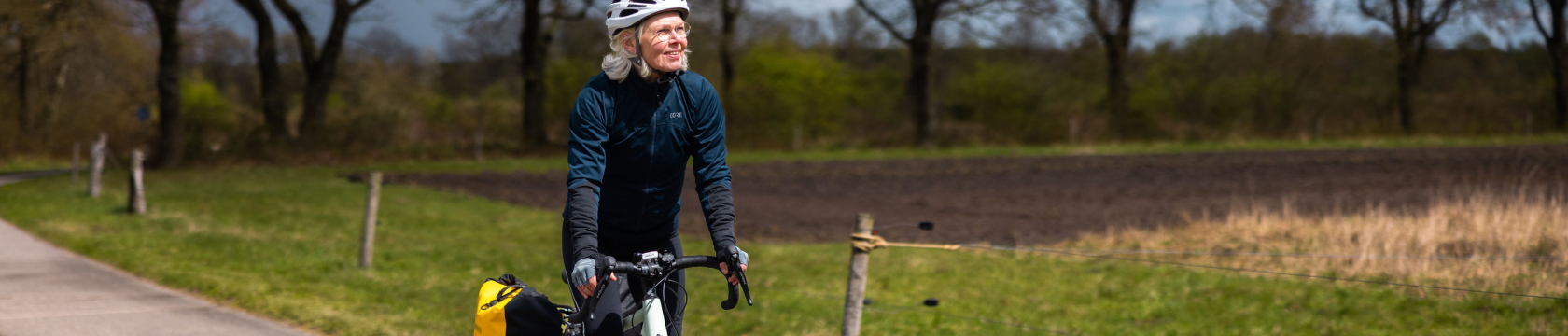 een oudere vrouw fietst door het Nederlandse landschap