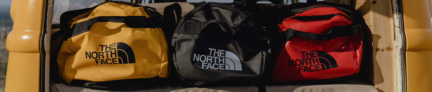 drie duffels van The North Face liggen in de kofferbak van een bus