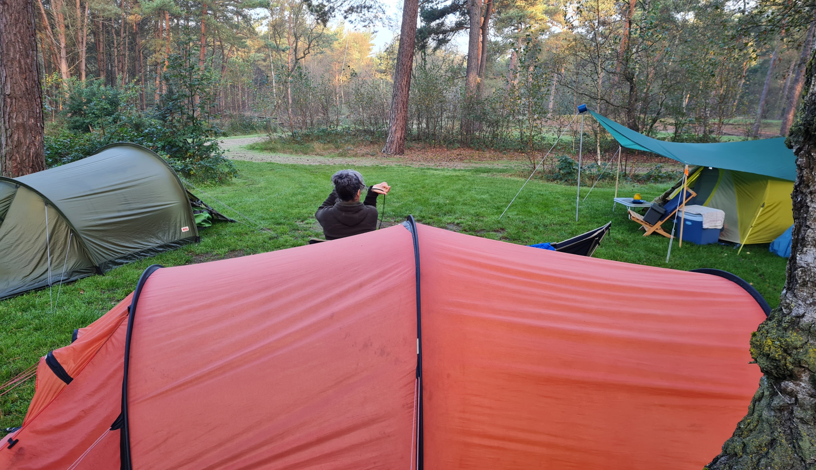 Een man zit voor zijn rode tent op een kampeerveld