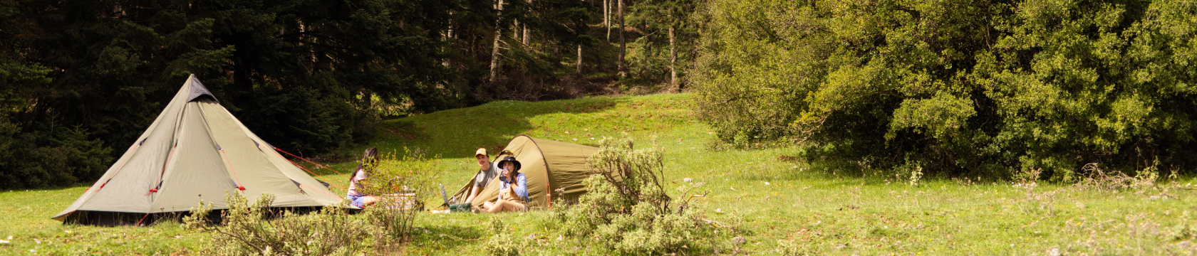 Drie mensen voor hun tent genieten van de zon