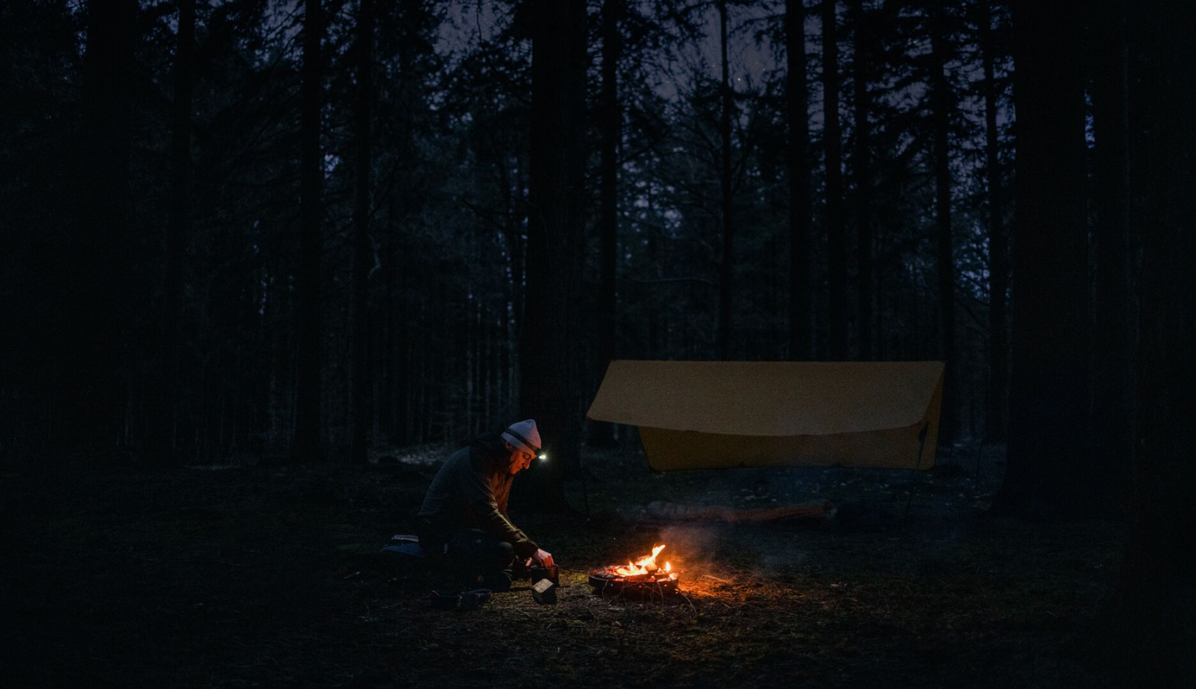 Een man zit bij een kampvuur in een donker bos