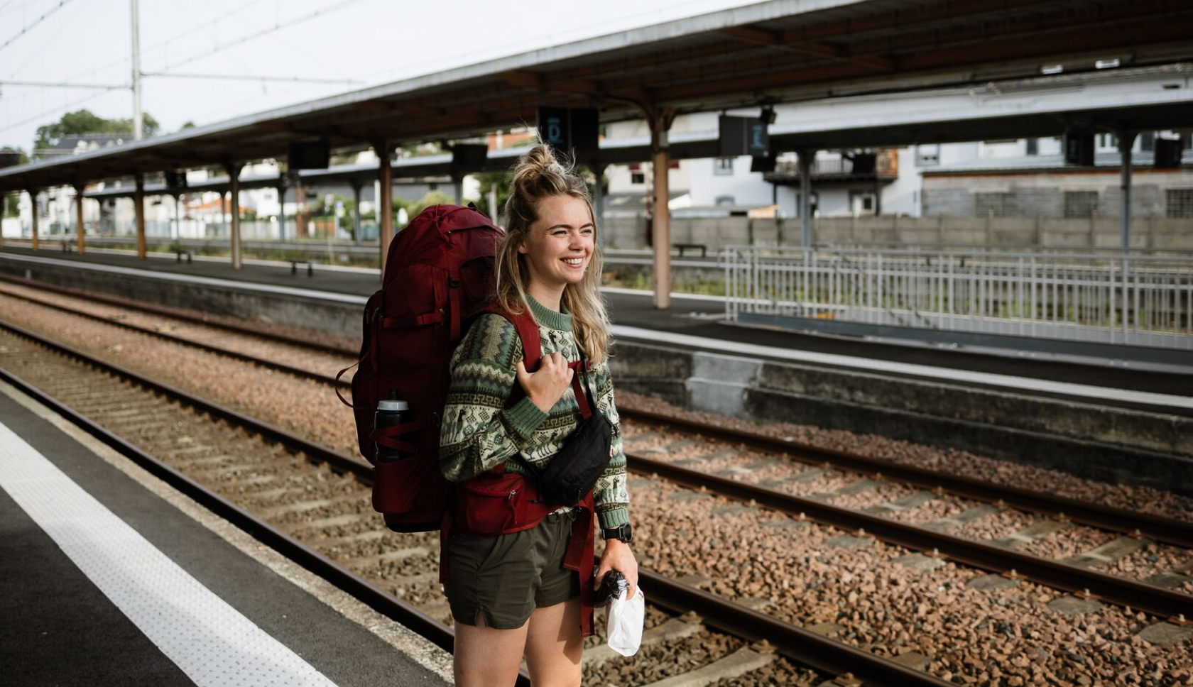 Een vrouw met een rode backpack staat op het station