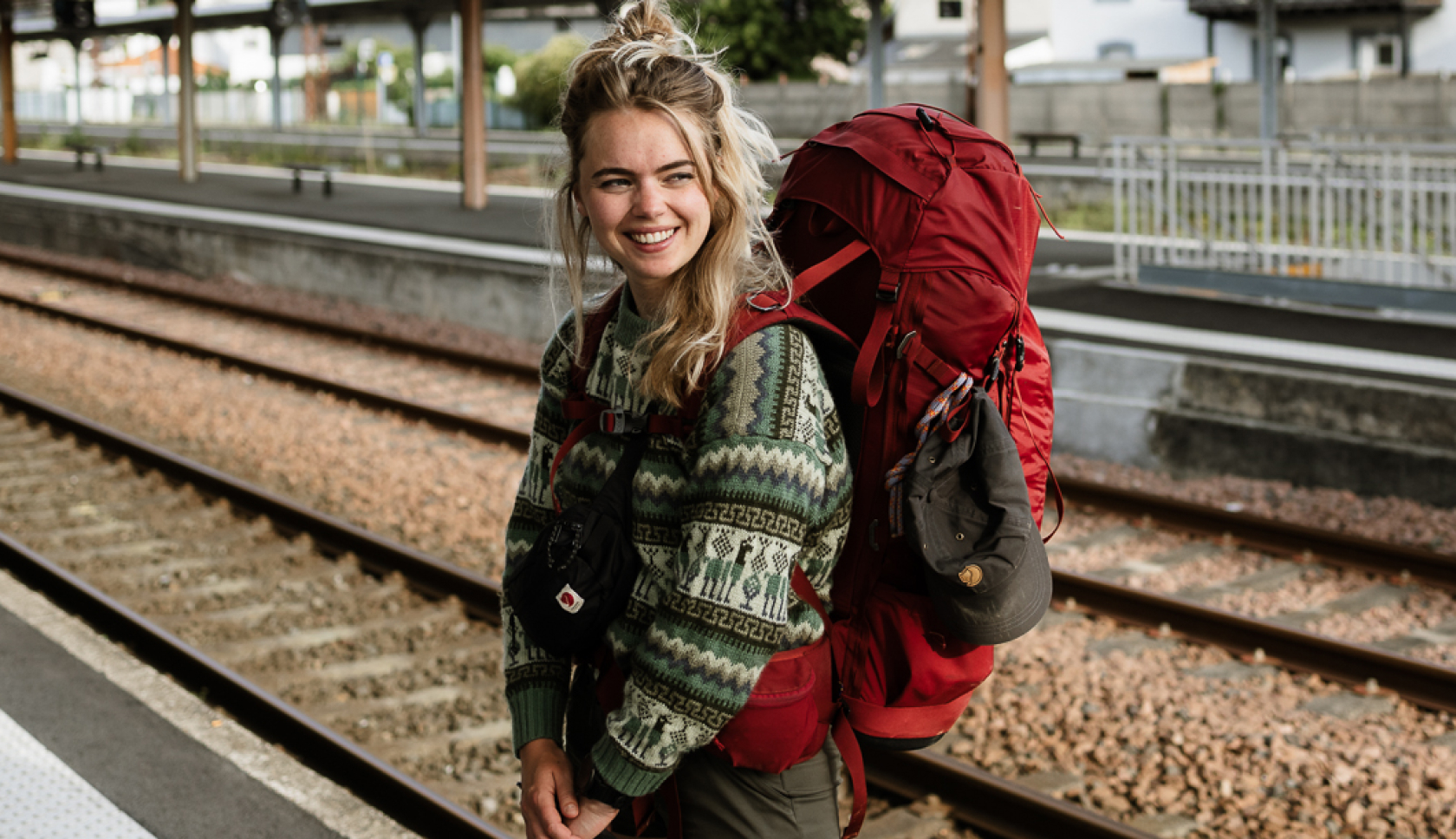 Een jonge vrouw met een rode backpack staat op een station