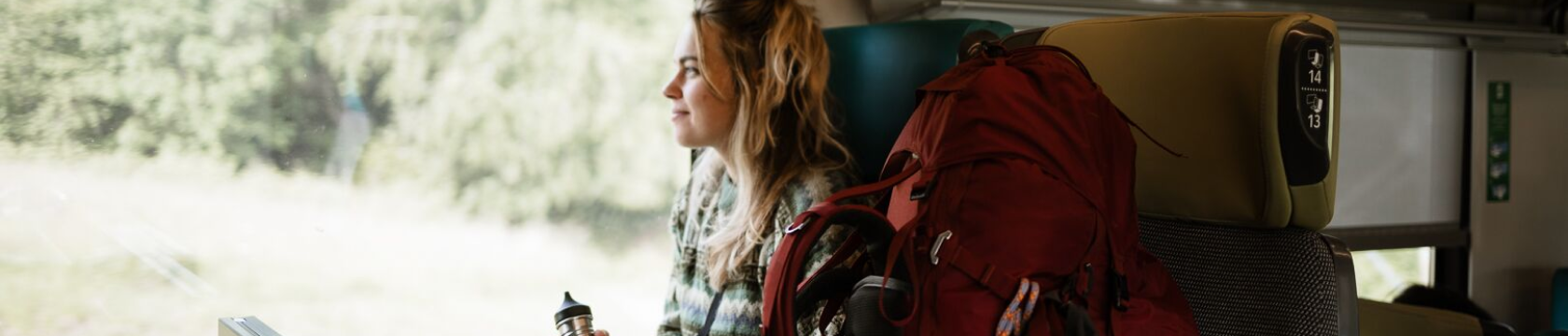 Een jonge vrouw zit in de trein met een rode backpack naast haar