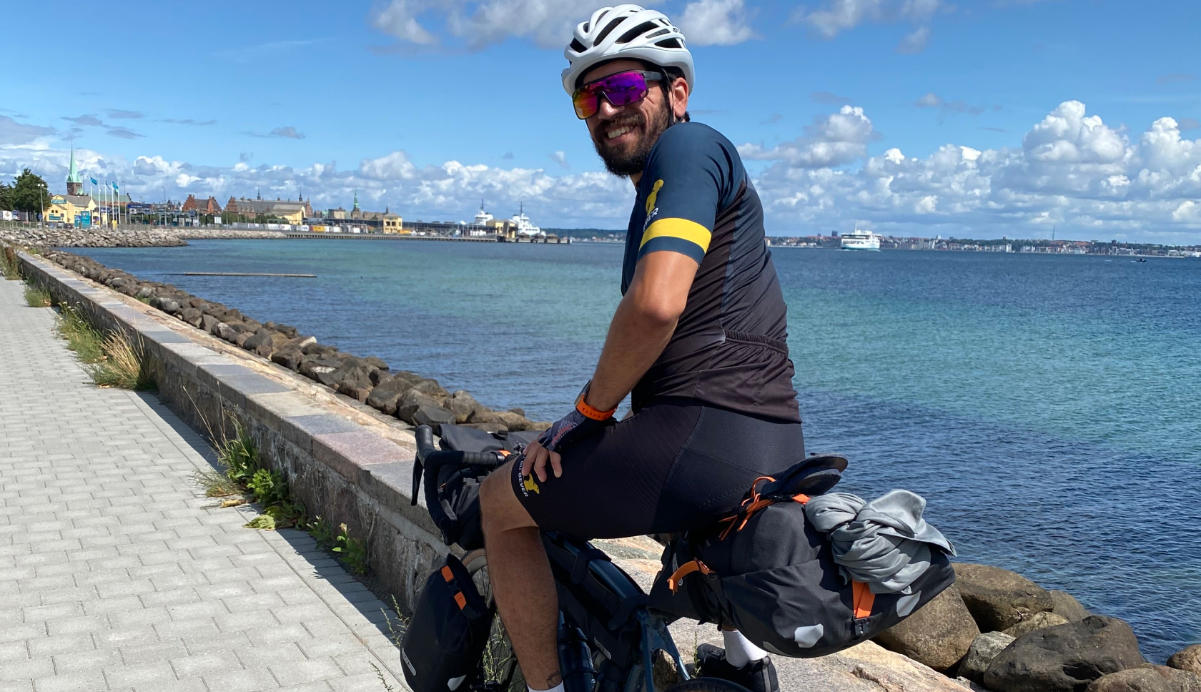 Buitenexpert Andres zit op de fiets aan het water en lacht in de camera