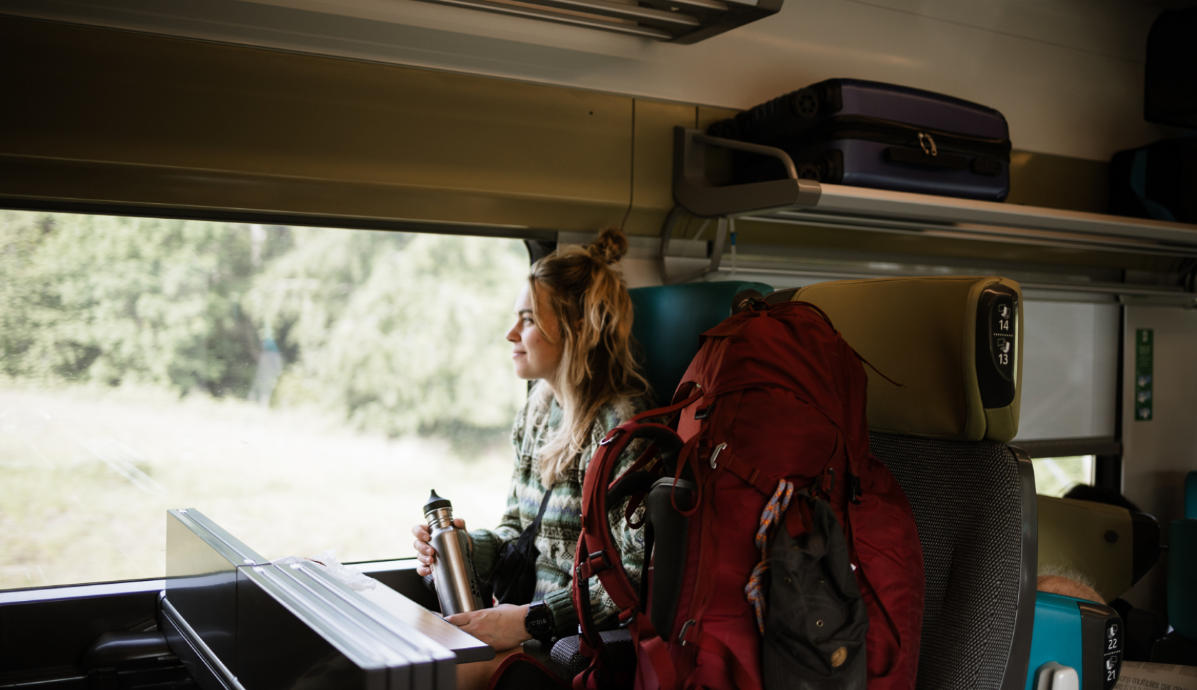 Een vrouw zit in een trein met een grote, rode backpack naast zich