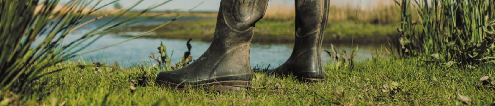 Iemand staat met laarzen in het gras bij een meer