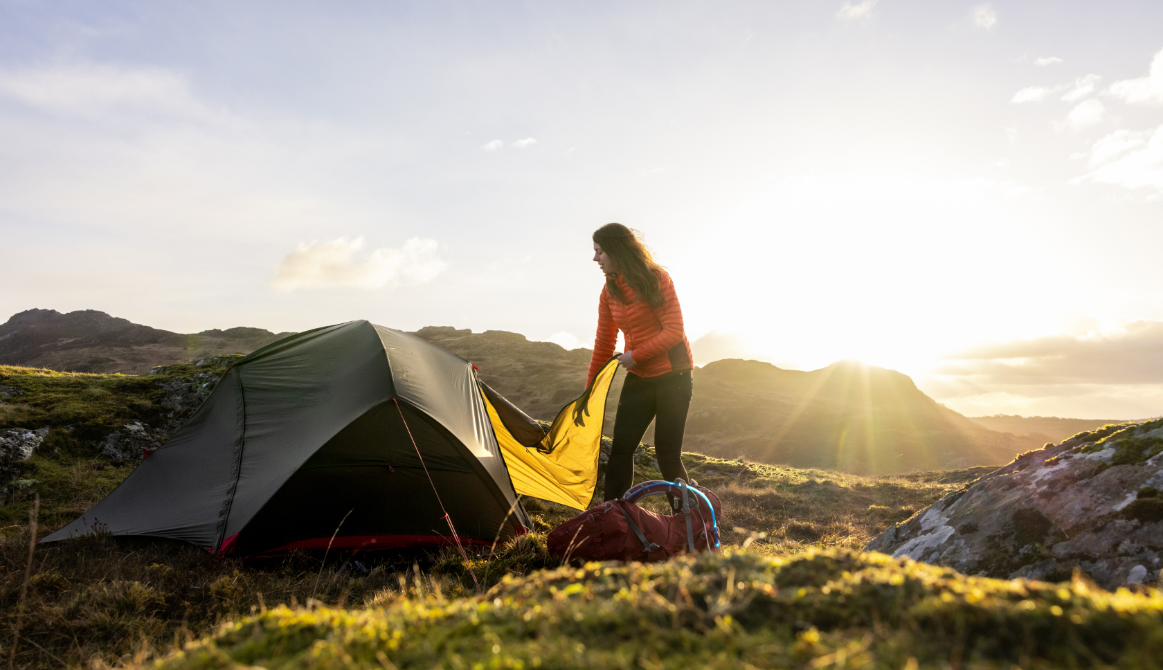 Een jonge vrouw zet haar tent op bij zonsondergang in de bergen