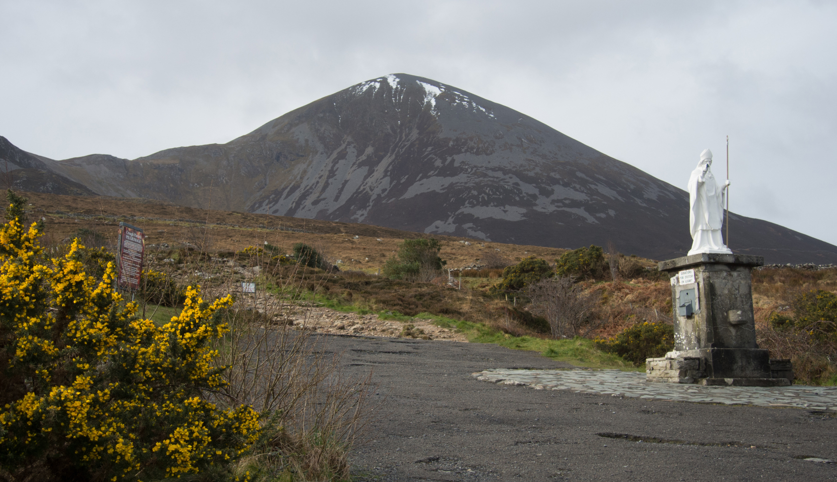 Wit standbeeld van de heilige Croagh Patrick met daarachter een besneeuwde bergtop