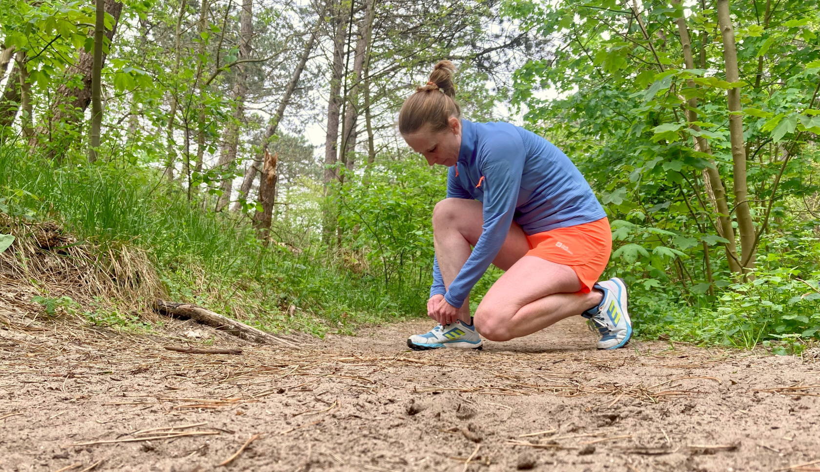 Een vrouw strikt haar hardloopschoenen in het bos op een zandpad