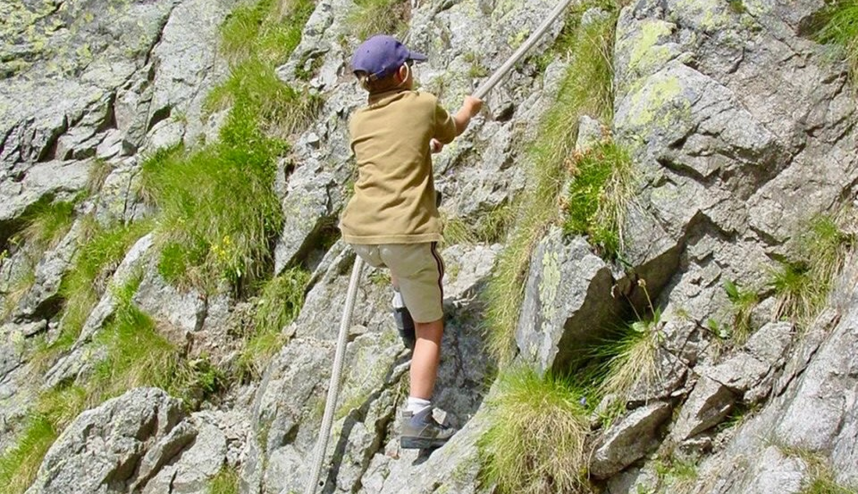 een jongen trekt zich aan een touw de berg op