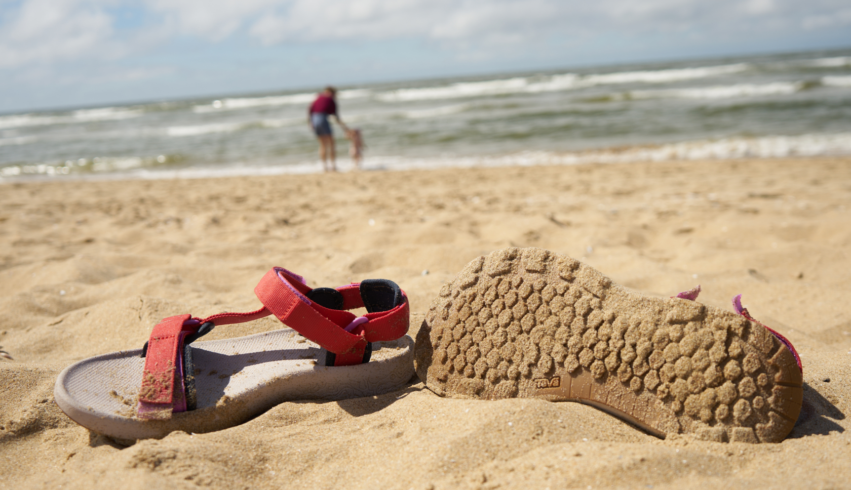 de zolen van sandalen gefotografeerd, op de achtergrond zie je de zee en het strand