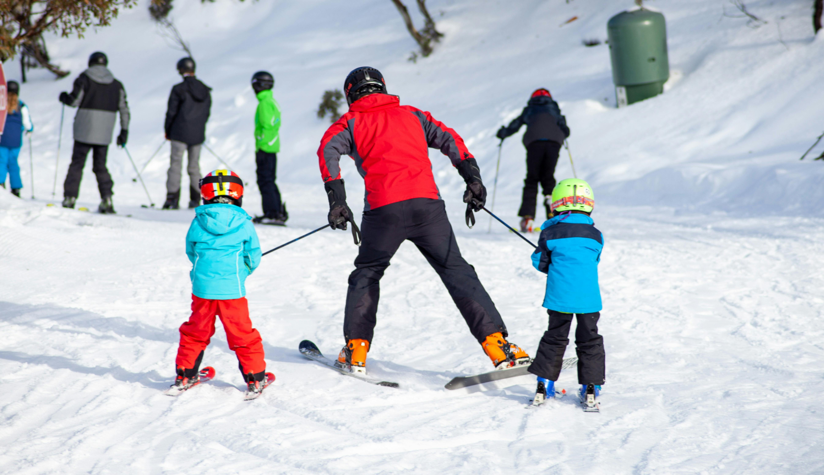 een persoon neemt twee kinderen mee de skipiste af