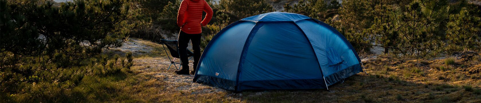 Een man staat voor zijn tent en kijkt uit over een mooi landschap