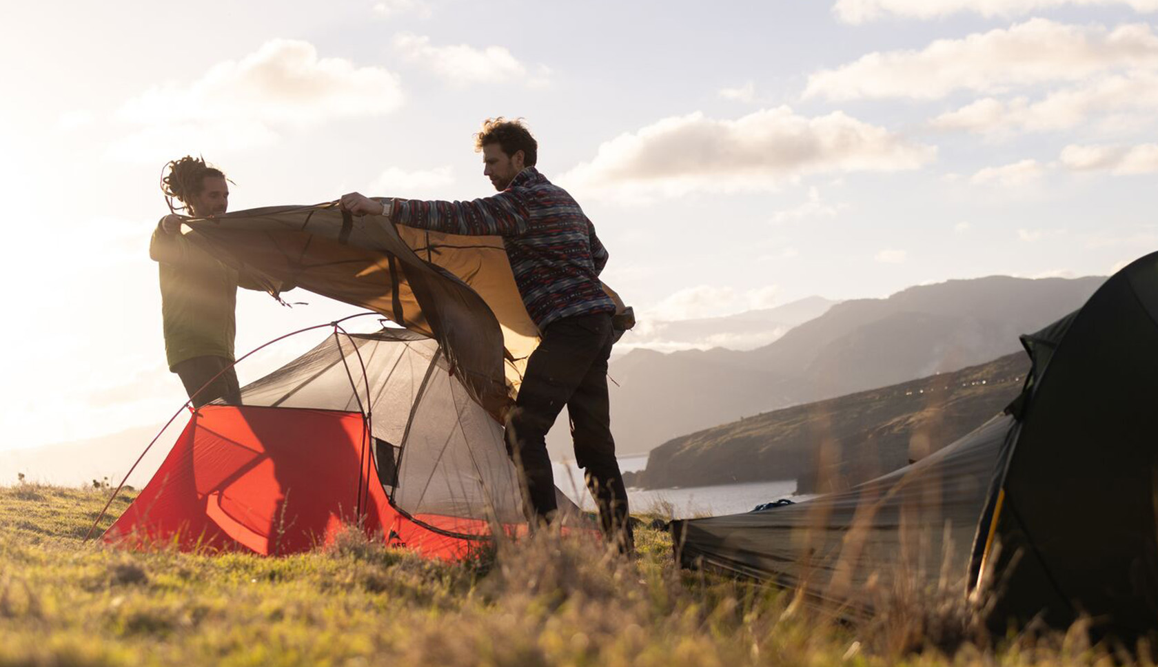 Twee mannen zetten hun tent op terwijl de zon bijna onder gaat.