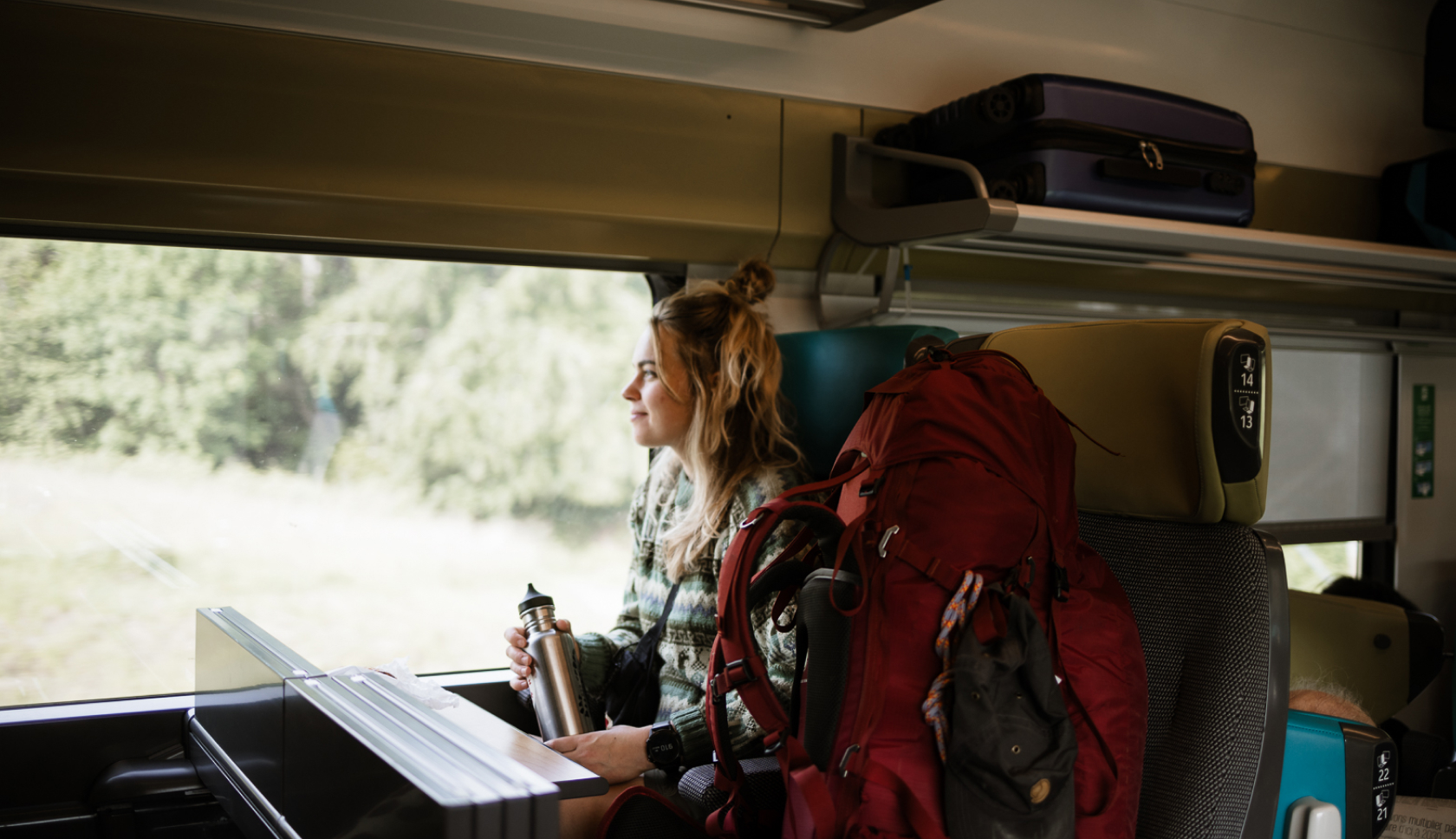 jonge vrouw zit in de trein met een rode backpack op de stoel naast haar