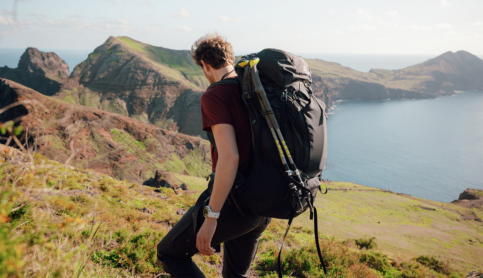 Man loopt met grote trekking-rugzak door een heuvelachtig landschap