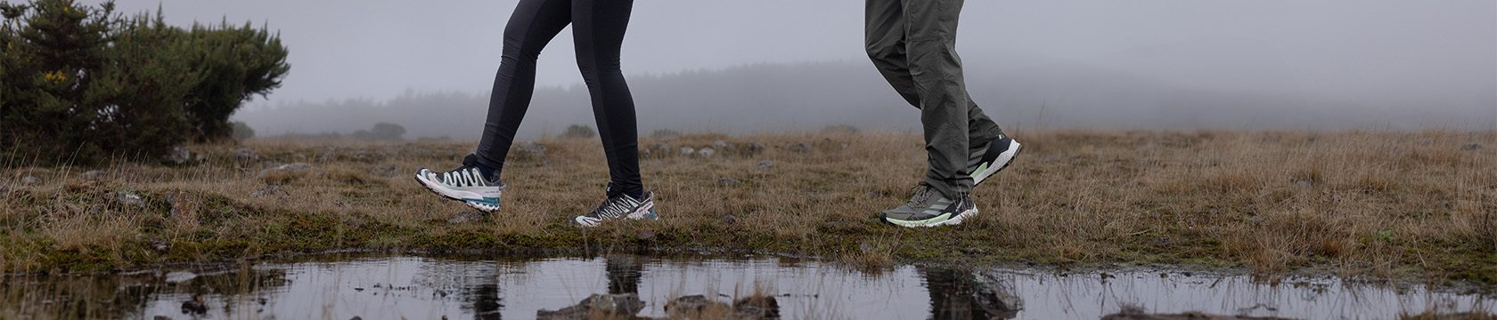 Twee paar wandelschoenen die door een nat natuurgebied lopen.