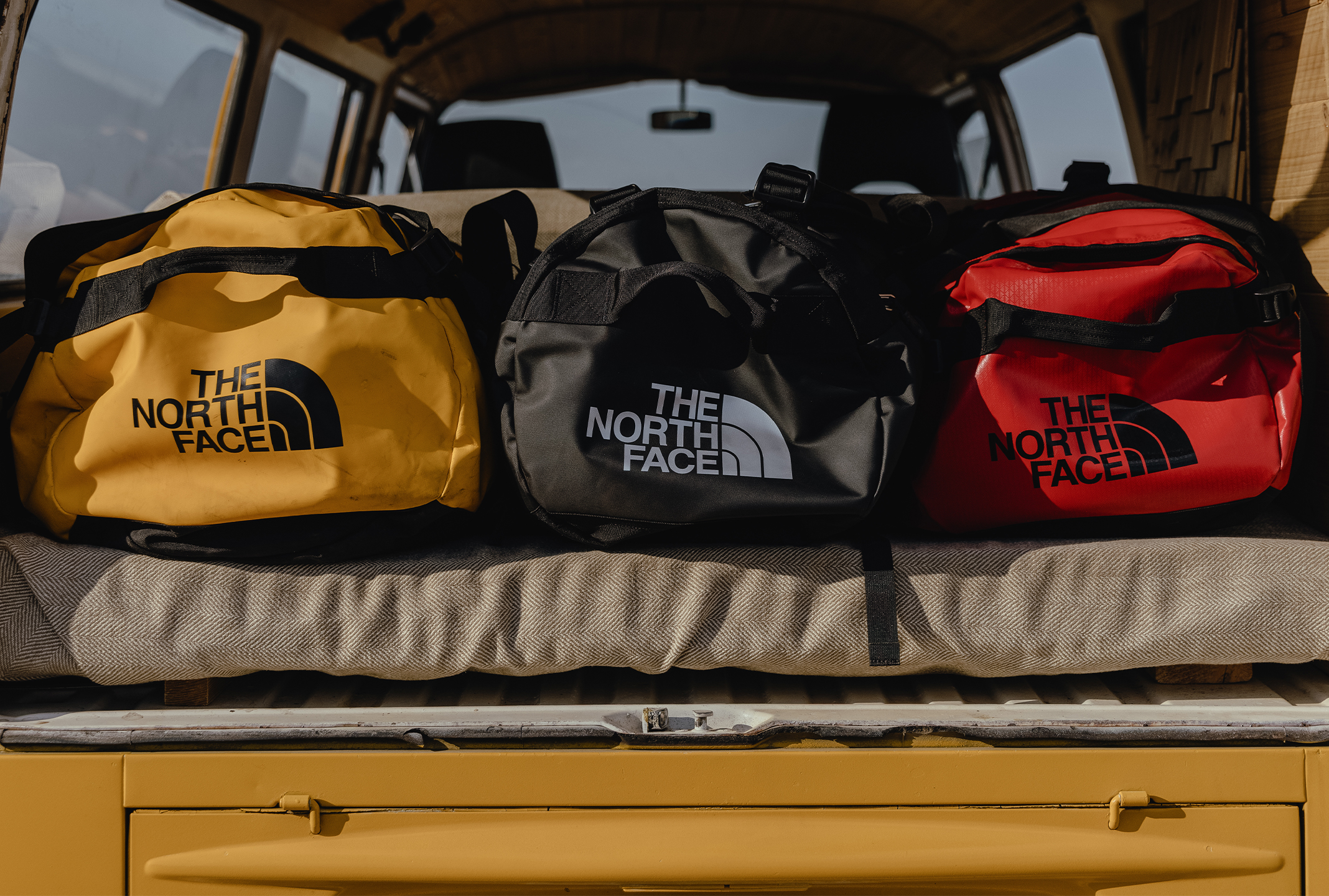 Drie duffels van The North Face liggen op de achterbank van een auto, klaar om op avontuur te gaan