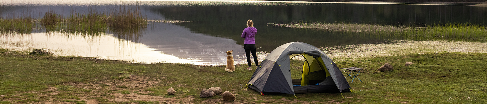 Vrouw en hond kijk uit over een meer, terwijl hun tent al is opgezet voor de nacht